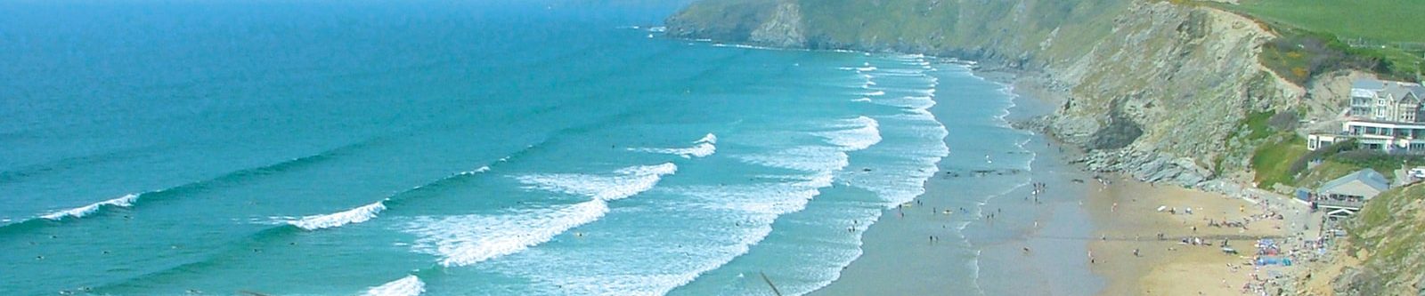 Watergate Bay beach with pink flowers on cliffs