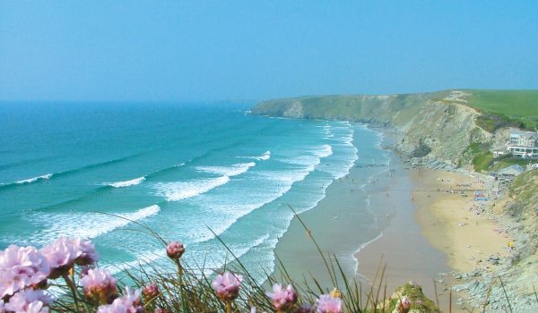 Watergate Bay beach with pink flowers on cliffs